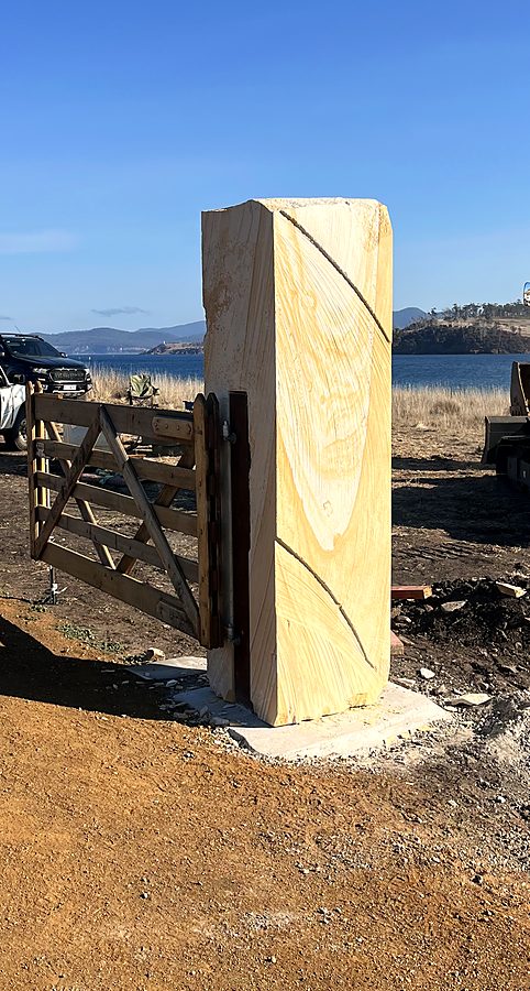 Carved sandstone gate post beside a timber gate, water beyond