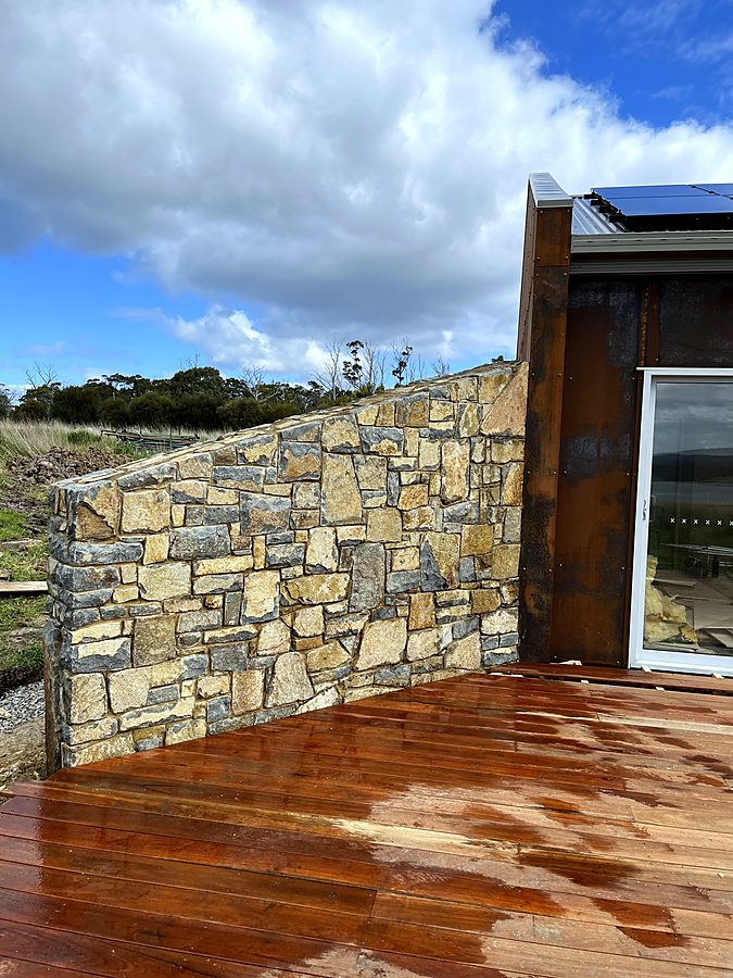 Raking stone wall meeting corten steel above a timber deck