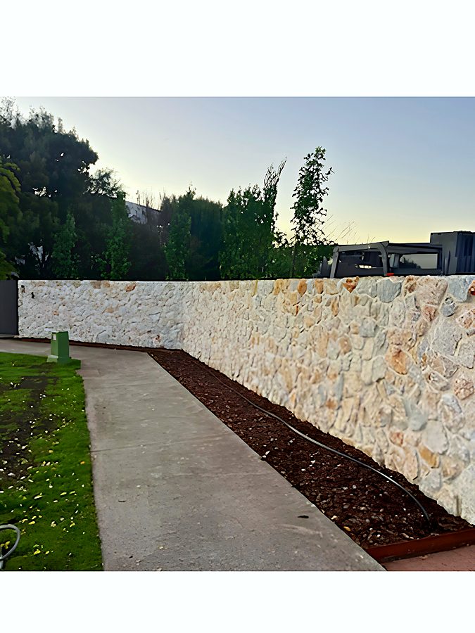 Rendered stone boundary wall alongside a concrete path at dusk