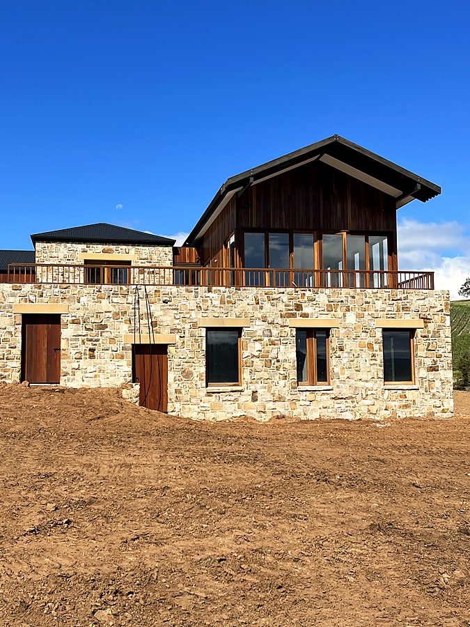 Two-storey natural stone house with timber gable above a vineyard