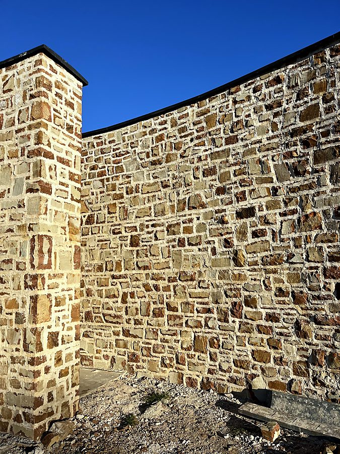 Stone pillar meeting a curved sandstone wall in raking light